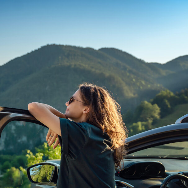 young woman standing next to a car in the mountains